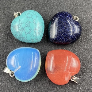 Assorted heart crystal pendants in turquoise, goldstone, and opal on dark surface