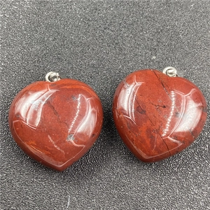 Detail of red jasper heart pendants with silver bails on a textured background