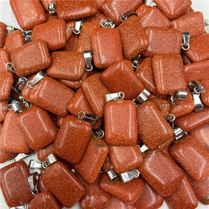 Close-up of sparkling goldstone rectangle pendants with silver metal bails on white backdrop