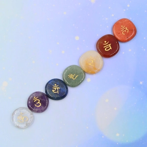 Set of seven natural chakra energy stones with engraved gold symbols on starry background
