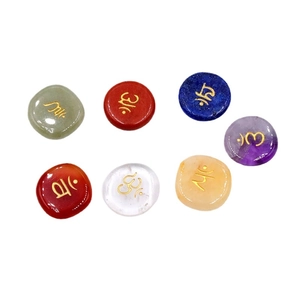 Set of seven natural chakra energy stones with engraved gold symbols on white background
