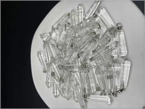 Macro view of clear crystal hexagonal prism pendants with silver metal clasps in a pile