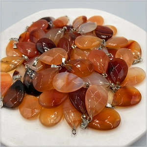 Polished faceted teardrop agate pendants in red and orange with silver clasps on a white plate