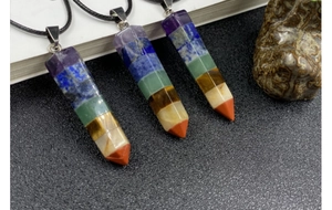Detail of three 7 Chakra healing crystal hexagonal pillar necklaces on a rustic stone background