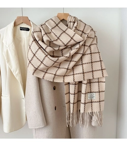 Detail of beige plaid scarf with fringe edge hanging on a minimalist clothing rack