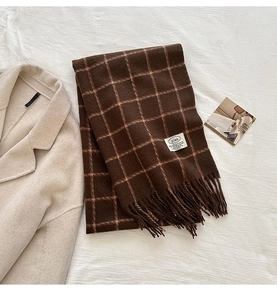 Detailed view of brown and orange plaid scarf with fringe tassels on a beige wool coat