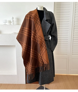Detail of a thick plaid scarf with tassels styled on a coat in a cozy home setting