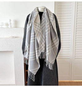 Detailed texture of thick plaid cashmere-like scarf with long fringe on grey coat