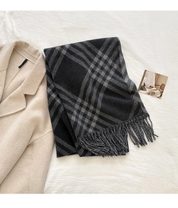 Detail of grey plaid scarf with soft fringe edges laid on a warm woolen coat
