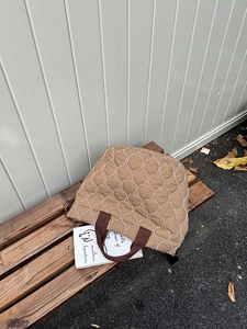 Detailansicht einer khakifarbenen Stepptasche mit weißen Wellennähten auf einer Holzbank