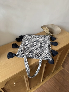 Detail of ethnic canvas tote with woven patterns and large deep blue tassels on wood