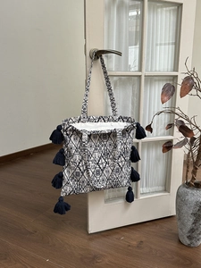 Detail of canvas tote with geometric print and dark blue tassels on a white door