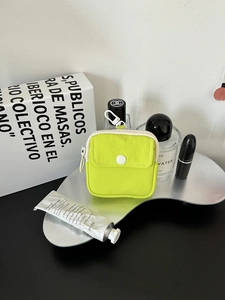 Detail of neon green mini pouch with white zipper and hook on a silver metal tray