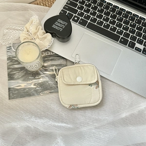 Close-up of cream quilted mini pouch for earbuds with metal carabiner on a desk