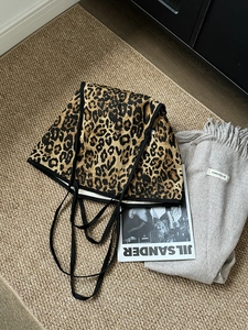 Detailed top view of leopard print canvas tote bag on a textured rug with fashion props