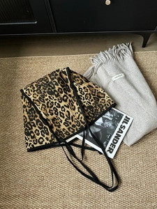 Detail of leopard print canvas tote bag with black strap handles on a textured carpet