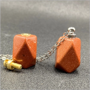 Dettaglio macro di un ciondolo boccetta di profumo in pietra d'oro con tappo a vite argento