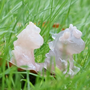 Hand-carved natural sakura agate monster figurines in pink and smoky grey on green grass