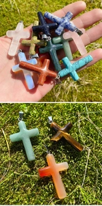 Detailed close-up of colorful natural gemstone cross pendants on green moss background