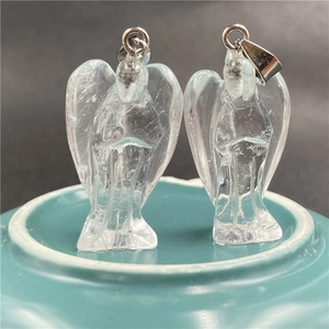 Detailed view of two clear crystal angel pendants with silver clasps on a blue base