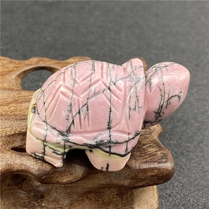 Macro detail of hand-carved pink rhodonite turtle gemstone with decorative wooden stand