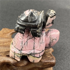 Macro shot of hand-carved rhodonite turtle duo on a traditional wood base display
