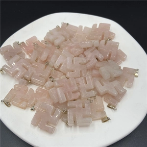 Close-up of pink quartz Swastika symbol charms with metal loops in a white tray