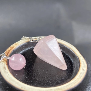 Macro detail of hexagonal pink quartz pendulum with metallic chain and natural ice textures