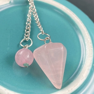 Macro shot of natural rose quartz pendulum with silver chain on a ceramic tray