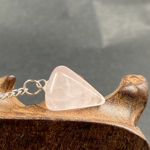 Close-up of hexagonal pink quartz crystal pendulum with silver chain on wood