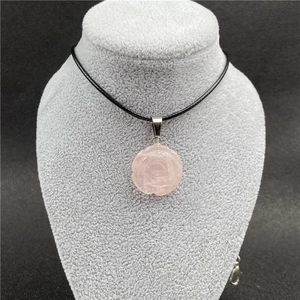 Gros plan d'un pendentif en quartz rose sculpté sur un cordon noir tressé en exposition
