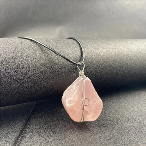 Raw rose quartz crystal necklace with silver wire wrap and black cord on grey background