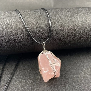 Macro detail of handmade wire-wrapped raw rose quartz crystal pendant on black cord