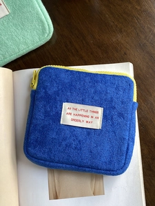 Close-up of blue terry cloth coin purse with yellow zipper and woven label