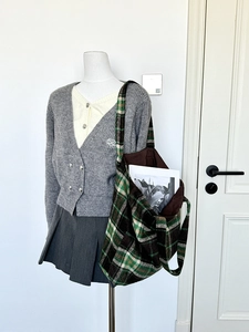 Detail of green plaid woolen tote bag styled with a gray knit cardigan and pleated skirt