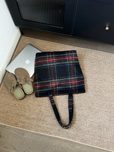 Flat lay of a large woollen tote bag with colorful plaid pattern on woven carpet