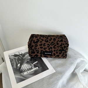 Close-up of leopard print corduroy makeup bag with woven label on a soft fabric surface