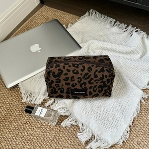Detail of leopard print corduroy cosmetic bag with zipper and logo patch on desk