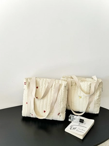 Detail of cream quilted tote bags with cherry and floral embroidery on a black table