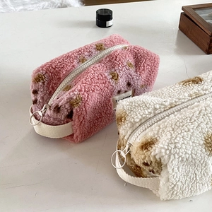Plush lamb wool cosmetic bags with heart patterns in pink and off-white on white desk