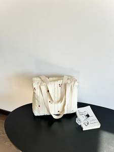 Close-up of quilted off-white tote bag with cherry print on a black round table