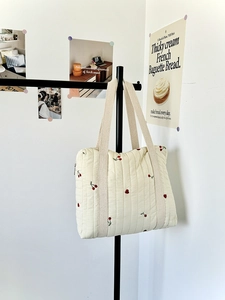 Detail of quilted beige tote bag featuring red cherry embroidery and wide woven straps