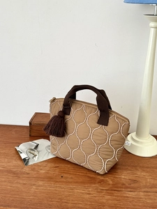 Borsa trapuntata color latte con cuciture rosa e nappa marrone su tavolo in legno