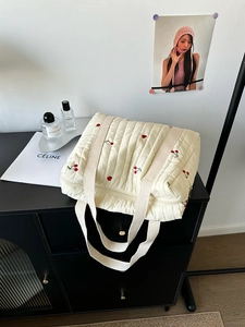 Detail of quilted cotton tote bag featuring red cherry embroidery and beige webbing straps