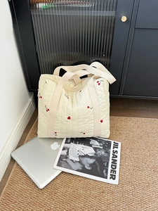 Close-up of quilted beige tote bag with red cherry embroidery on a textured mat