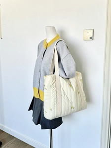 Quilted tote bag with yellow floral embroidery and canvas strap on a mannequin