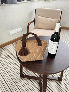Borsa tote trapuntata kaki con cuciture a onda, ciondolo a nappa e chiusura a zip sul tavolo