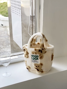 Detail of white faux fur bucket bag featuring brown teddy bear print and Good Luck label
