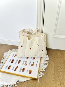 Detail view of cream quilted tote bag with red cherry embroidery on a woven rug