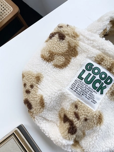 Close-up of fluffy white teddy bucket bag featuring brown bear patterns and Good Luck label